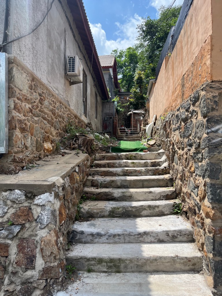 石造りの階段がある狭い路地。両側には家が並び、青空が広がっている。