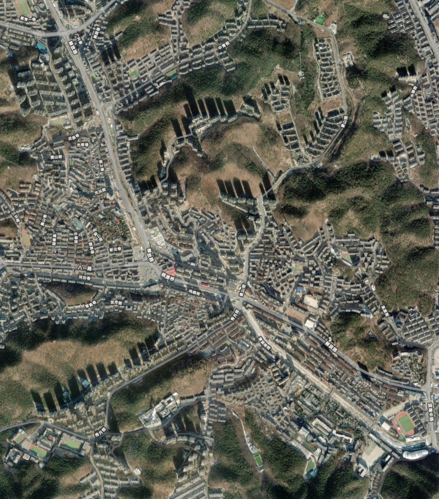 城市の航空写真。住宅街、道路、山が見える。